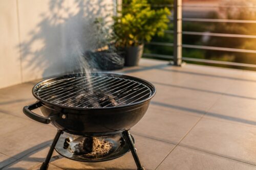 Petit barbecue rond au charbon posé sur une terrasse avec un léger filet de fumée